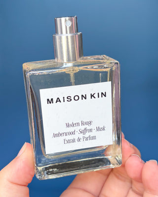 Maison Kin perfume bottle and packaging on a wooden surface with a blue background