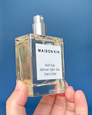 Maison Kin perfume bottle held in hand against a blue background