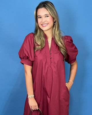 A woman modeling a short-sleeve burgundy puff-sleeve tunic dress with a buttoned collar
