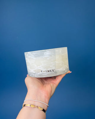 Thymes Frasier Fir Tidings 21 oz. marbled glass candle displayed on a solid blue background. 