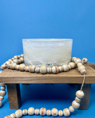 Thymes Frasier Fir Tidings 21 oz. marbled glass candle displayed on a solid blue background. 