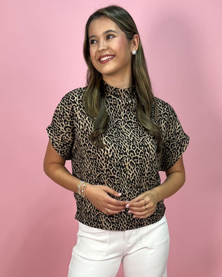Woman wearing a leopard print top and white pants against a pink background