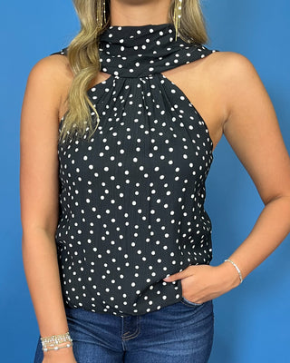 Black and white polka dot sleeveless top with a draped high neckline, gathered detail, and relaxed fit.