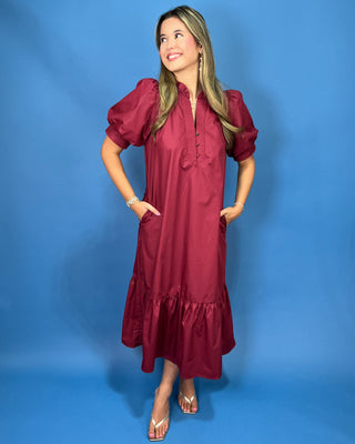 A woman modeling a burgundy midi dress with puff sleeves, a gathered neckline, and a ruffled hem