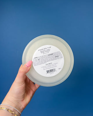 Thymes Frasier Fir Tidings 21 oz. marbled glass candle displayed on a solid blue background. 
