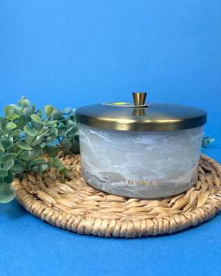 Thymes Frasier Fir Tidings 21 oz. marbled glass candle displayed on a solid blue background. 