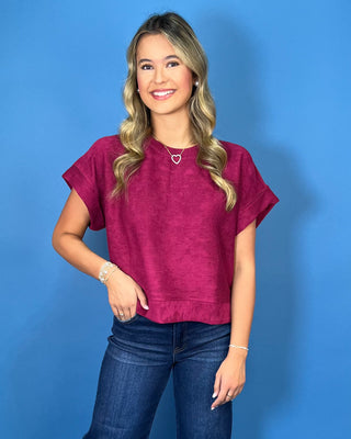 Berry magenta short sleeve top with a round neckline, relaxed fit, cuffed sleeves, and subtle textured fabric.