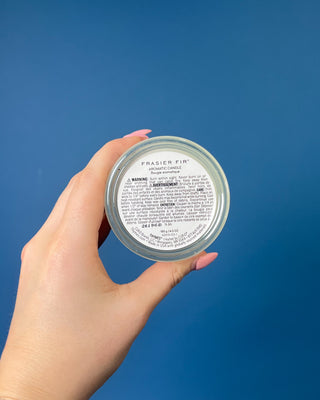 Thymes Frasier Fir Tidings 6.5 oz. candle in decorative gift box displayed on a solid blue background. 