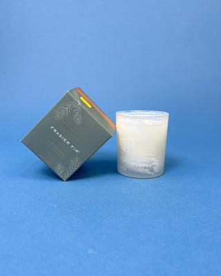 Thymes Frasier Fir Tidings 6.5 oz. candle in decorative gift box displayed on a solid blue background. 