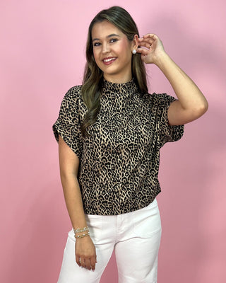 Woman wearing a leopard print top and white pants against a pink background