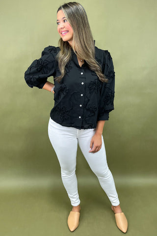 Woman wearing a black blouse with ruffled sleeves and white pants on a green background