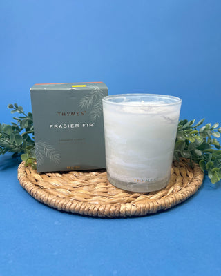 Thymes Frasier Fir Tidings 13 oz. candle in a decorative gift box displayed against a solid blue background. 