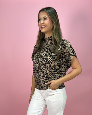 Woman wearing a leopard print top and white pants against a pink background