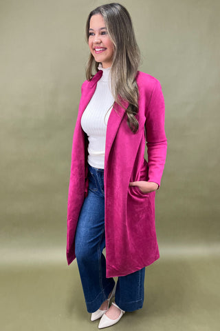 Woman wearing a bright pink coat over a white top and blue jeans on a beige background