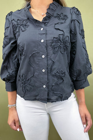 Dark blue blouse with floral embroidery worn by a person on a green background