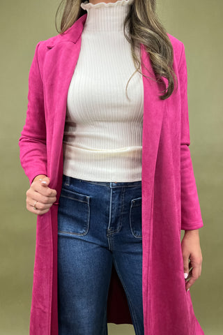 Person wearing a bright pink coat over a white sweater and blue jeans on a green background