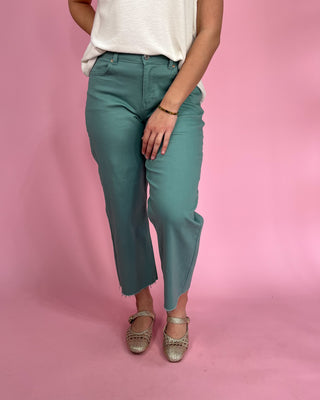 Person wearing teal pants and a white top on a pink background