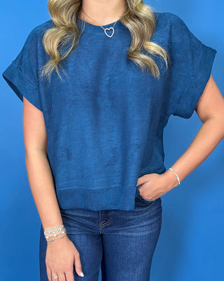 Deep teal blue short sleeve top with a round neckline, cuffed sleeves, relaxed fit, and subtle textured finish.