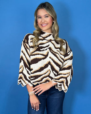 Brown, ivory, and tan zebra print mock neck sweater with bell sleeves, relaxed fit, and scalloped hem detailing.