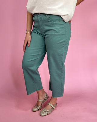 Person wearing teal pants and white top on a pink background