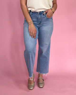 Person wearing blue jeans and gold sandals on a pink background