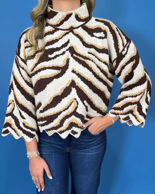 Brown, ivory, and tan zebra print mock neck sweater with bell sleeves, relaxed fit, and scalloped hem detailing.
