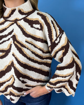 Brown, ivory, and tan zebra print mock neck sweater with bell sleeves, relaxed fit, and scalloped hem detailing.