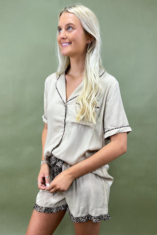 Woman wearing a beige pajama set with lace trim against a green background