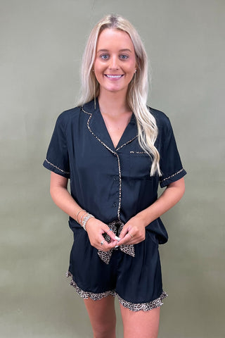 Woman wearing a black outfit with decorative trim against a plain background
