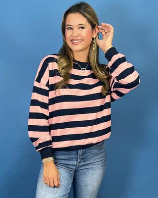 A woman modeling a pink and navy blue horizontally striped long-sleeve sweatshirt, paired with blue jean