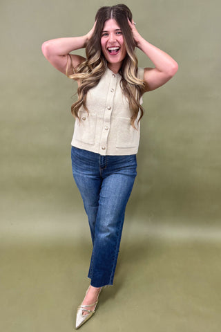 Woman wearing a beige top and blue jeans against a green background