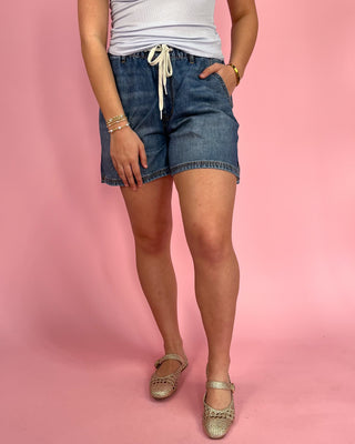 Person wearing blue denim shorts on a pink background