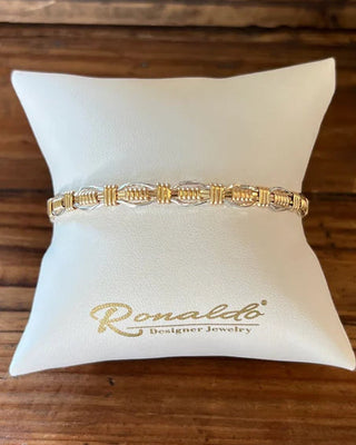 Gold bracelet on a white pillow with 'Ronald' branding on a wooden surface