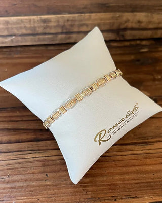 Gold bracelet on a white pillow with 'Romantic' branding on a wooden surface