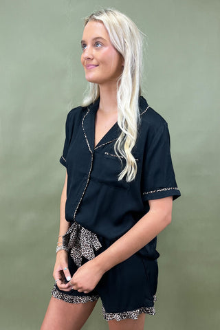 Woman wearing a black outfit with leopard print trim against a green background