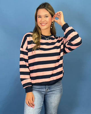 A woman modeling a pink and navy blue striped long-sleeve knit sweater, paired with light-wash blue jeans and metallic gold flats
