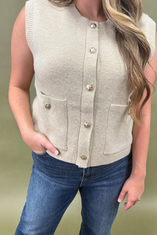 Person wearing a beige button-up vest over a blue top with a plain background