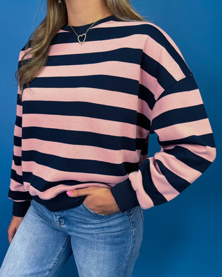 A woman wearing a pink and navy blue horizontally striped long-sleeve sweatshirt with blue jean