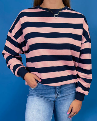 A person wearing a long-sleeve crewneck sweatshirt with horizontal pink and navy stripes, paired with light blue jeans