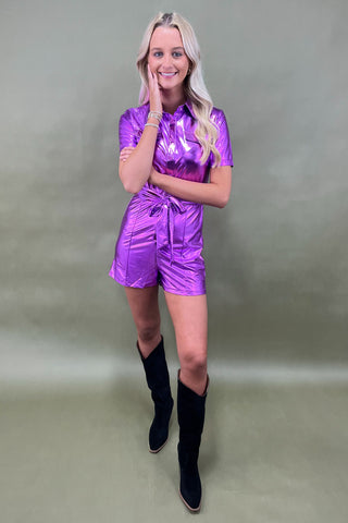 Woman wearing a shiny purple outfit with black boots against a plain background