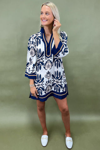 Woman wearing a white dress with blue patterns against a green background