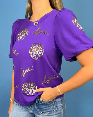 a purple short-sleeve t-shirt with gold and white graphics, paired with blue jeans