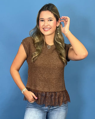 A woman modeling a brown short-sleeve knit top with a ruffled hem, paired with light-wash blue jeans
