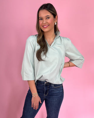 Woman wearing a light blue shirt and dark jeans against a pink background