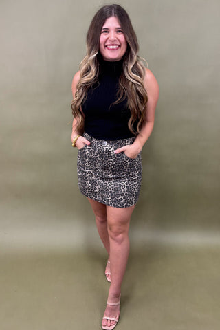 Woman wearing a black top and patterned skirt against a plain background