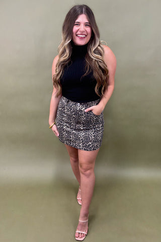 Woman wearing a black sleeveless top and patterned skirt against a green background