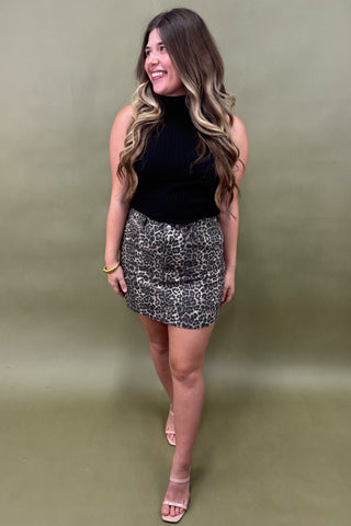 Woman wearing a black sleeveless top and leopard print skirt against a green background