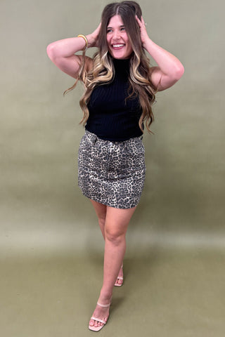 Woman wearing a black top and patterned skirt against a plain background