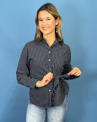 A woman modeling a navy blue and white vertically striped long-sleeve button-up shirt with a tie waist, paired with light-wash blue jean