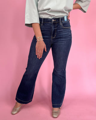 Person wearing blue jeans and a light gray shirt on a pink background